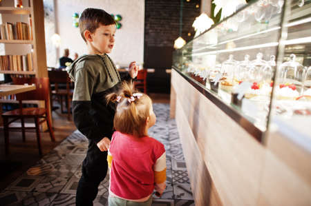 Brother with sister in cafe choose a dessert from shop window.の写真素材