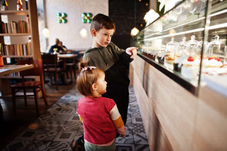 Brother with sister in cafe choose a dessert from shop window.の写真素材