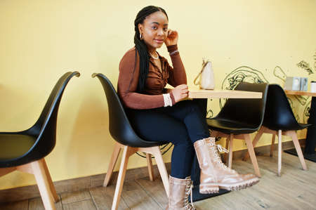 African american woman in brown shirt and black pants sit in cafe.の写真素材