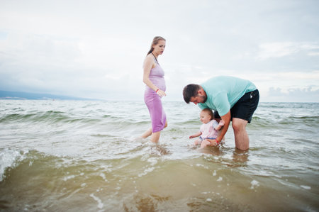 summer holidays. Parents and people outdoor activities with children. Happy family holidays. Father, pregnant mother, baby daughter on sea sand beach.の写真素材