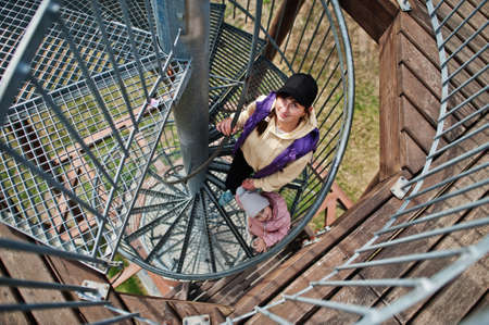 Mother with daughter stand at spiral staircase of wooden observation tower.