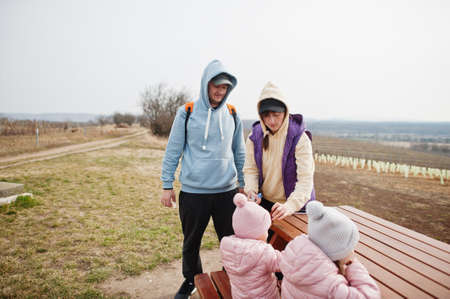 Family with children sit at wooden table against vineyard.