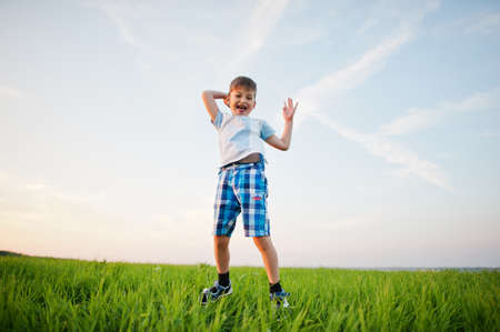 Cute jumping boy in green grass field at evening.の写真素材