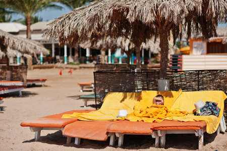 Boy lies on a sunbed on the shore of egyptian resort. Yellow towels.