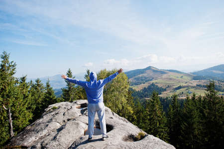 Happy hiker with hands in the air stand on rock. View over rocky valley.