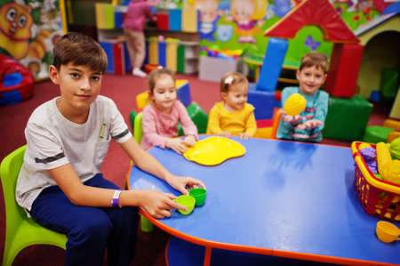 Four kids  playing in indoor play center. Kindergarten or preschool play room. Sitting by the table with plastic fruits.の写真素材