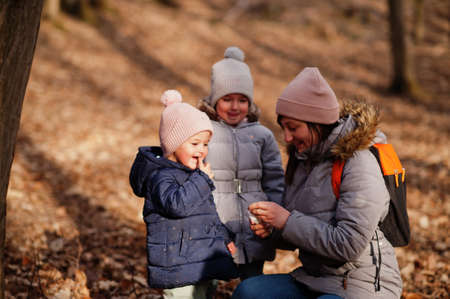 Mother with daughters wear jacket and hat in early spring forest.