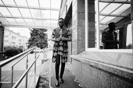 African stylish and handsome man in traditional outfit and sunglasses standing outdoor.の写真素材