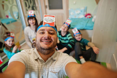 Happy family with four kids playing game guess who while having fun at home.