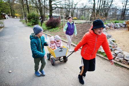 Mother with four kids discovering and watching animals at zoo. Boy pulls wooden trolley.の写真素材