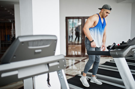 Fit and muscular arabian man running on treadmill in gym.
