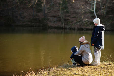 Mother with kids fishing with a stick in pound at early spring park.の写真素材