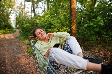 Boy sitting in trolley with mobile phone at forest.の写真素材