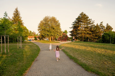 Back of two sisters run to playground in park.の写真素材