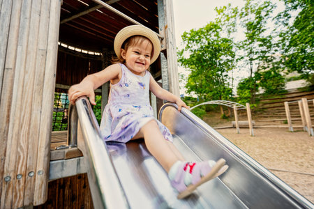 Baby girl slides in children's playground toy set in public park.の写真素材