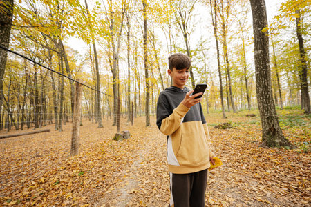 Teenage boy looking in mobile phone at autumn forest.の写真素材