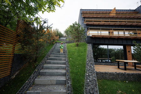 Baby girl walking on stairs against modern wood stone house.