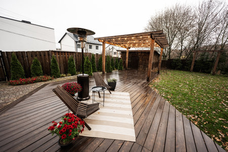 Stainless steel metal gas outdoor patio heater with wooden chairs and pot with flowers at wet...