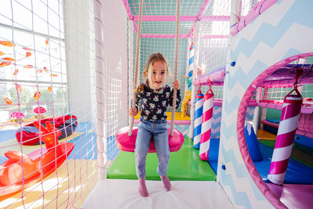 Happy sisters playing at indoor play center playground. Girl in swing.の写真素材