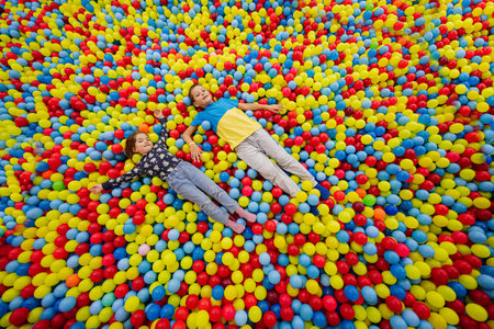 Brother with sister playing at indoor play center playground. Girl with boy lying at color balls in ball pool.の写真素材