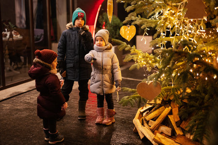 Three kids having fun near illuminated Christmas tree outdoor in evening.の写真素材
