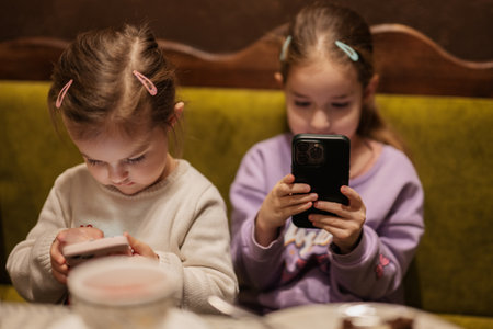 Sisters kids hold mobile phone together at cozy cafe and having fun.の写真素材