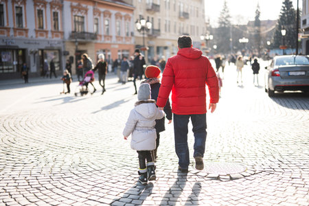 Back of grandfather with grandson and granddaughter walking  in city square.の写真素材
