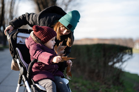 Young woman in city park with baby stroller. Warm autumn weather for outdoor activity.の写真素材