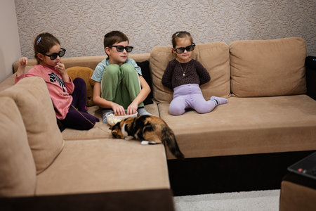 Three children sitting on the living room, wear 3d glasses watching movie or cartoon.の写真素材