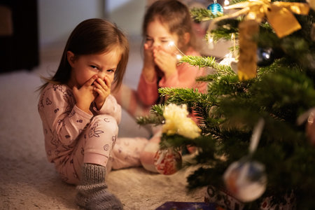 Two sisters together near Christmas tree at evening home.