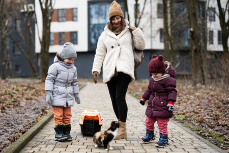Mother and daughters walking with kitten in travel plastic cage carriage outdoor at park.の写真素材