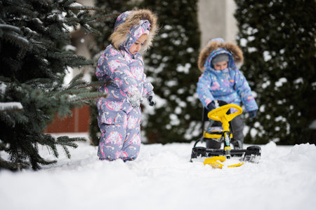 Children play outdoors in snow. Two little sisters enjoy a sleigh ride. Child sledding. Toddler kid riding a sledge. Kids sled in winter.の写真素材