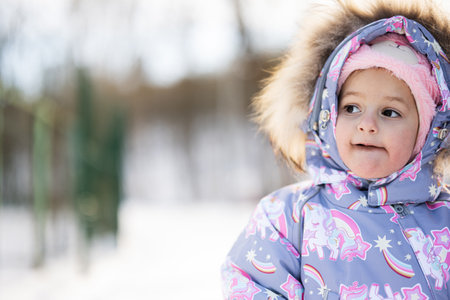 Close up portrait of baby girl wear child snowsuit on a sunny frosty winter day.