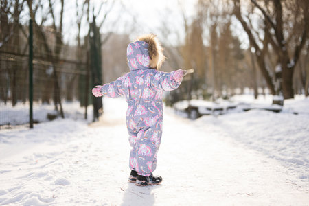 Back of baby girl wear child snowsuit on a sunny frosty winter day.