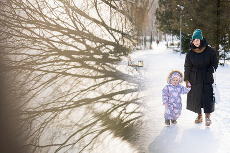 Mother and child walking on a sunny frosty winter day in the park. Reflection of trees.の写真素材