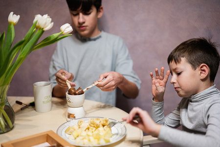 Children eat fruits and desserts, drink tea at home in the evening kitchen. Chocolate on a stick for melting.の写真素材