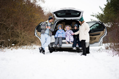 Family with kids sit on car suv with open trunk stand in winter forest.の写真素材