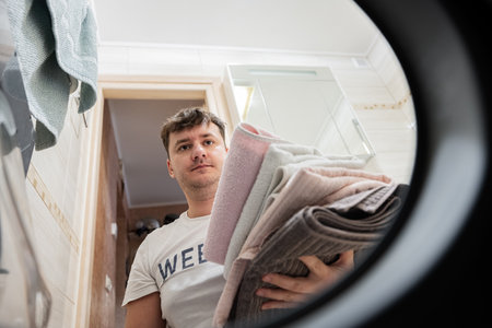 Man view from washing machine inside. Male does laundry daily routine.