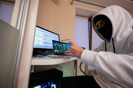 Boy hacker fraudulently use credit card for payment. Internet theft . Man wearing a balaclava and...