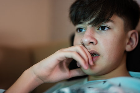 Young teen boy in front of a laptop on a bed at evening.の写真素材