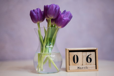 Hello spring! Wooden cubic calendar with date of 6 March surrounded with bouquet of purple tulips...