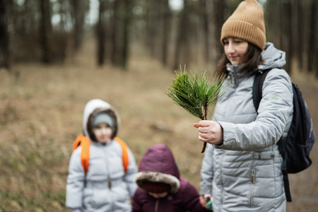 Mother shows a coniferous branch to the girls in forest.