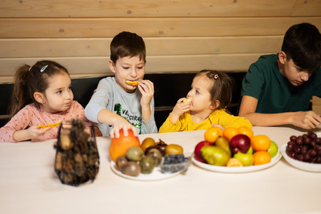 Four children eat fruits in wooden country house on weekend.の写真素材