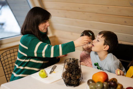 Mother with kids eat fruits in wooden country house on weekend.の写真素材