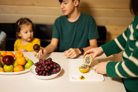 Mother with four children eat fruits in wooden country house on weekend. Mom cuts the yellow dragon fruit.の写真素材