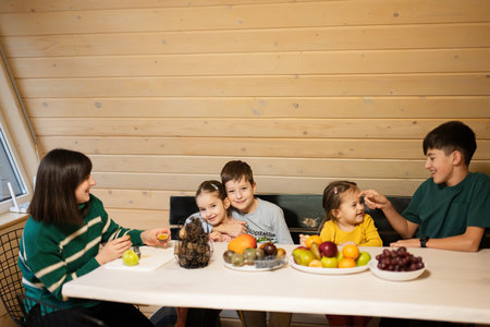 Mother with four children eat fruits in wooden country house on weekend.の写真素材