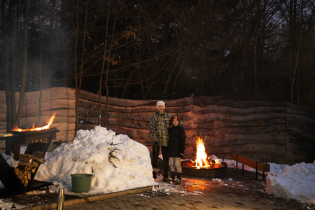 Two brothers stand together by the fire pit in winter night.の写真素材