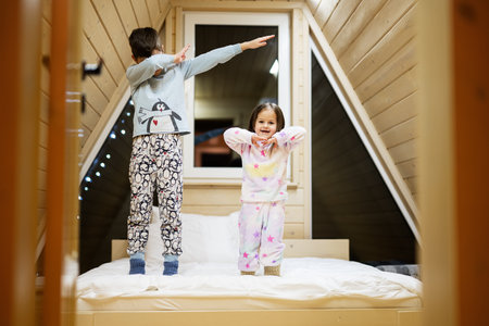 Children in soft warm pajamas playing at wooden cabin home. Concept of childhood, leisure activity, happiness. Brother and sister having fun and playing together.の写真素材