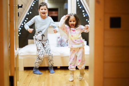 Children in soft warm pajamas playing at wooden cabin home. Concept of childhood, leisure activity, happiness. Brother and sister having fun and playing together.の写真素材