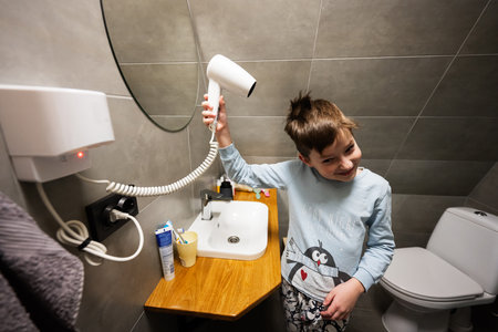 Boy dries hair with a hair dryer at bathroom.の写真素材
